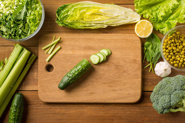Fresh gree vegetables for salad on a wooden table with a cutting board. Top view.
