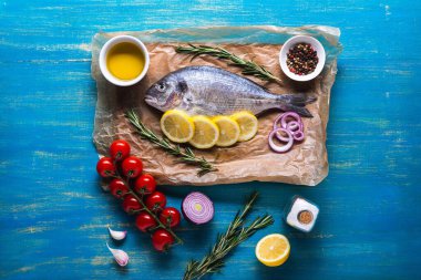 Dorado balığı kesim tahtası ve limon ve baharatlı parşömen kağıdı üzerinde pişirmeye hazır. Mavi ahşap bir arkaplanda üst görünüm.