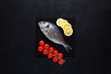 Taze Dorado siyah arka planda limon ve kiraz domatesli siyah bir taş kesme tahtasında pişirmeye hazır. Üst görünüm.