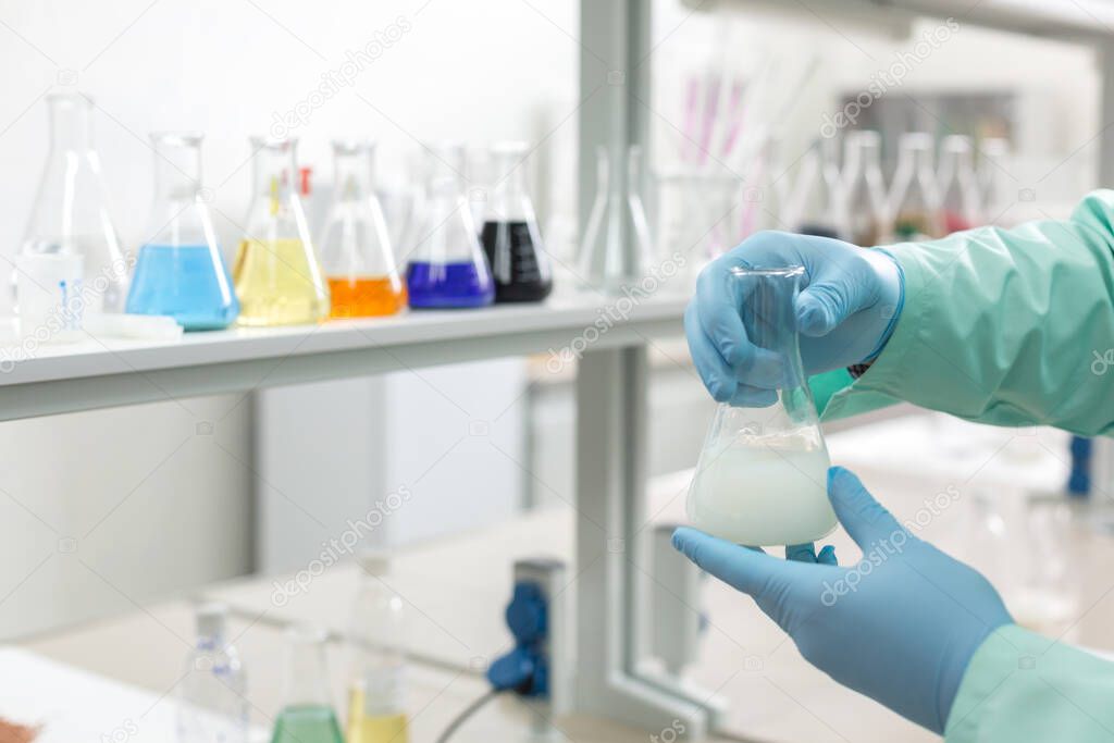 Hands in latex gloves holding flasks on the background of the shelves in the laboratory. Concept: Scientific research