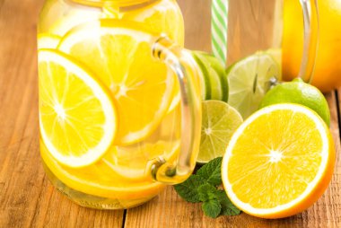 Two jars of detox water with slices of orange and lime close-up. Glass jar with handle stands on a wooden table.
