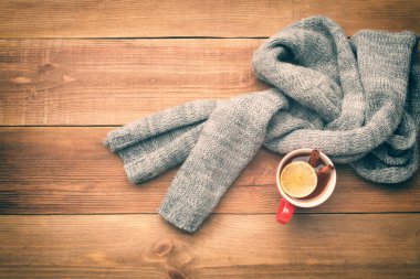 Bir fincan sıcak çay yünlü bir eşarba sarılır. Bardakta bir limon ve iki tarçın çubuğu var. Üst Manzara. Metin için boşluk.