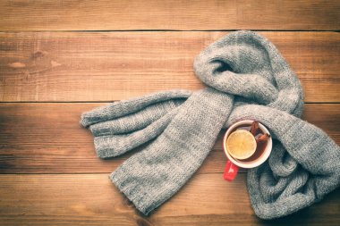 Bir fincan sıcak çay yünlü bir eşarba sarılır. Bardakta bir limon ve iki tarçın çubuğu var. Üst Manzara. Metin için boşluk.