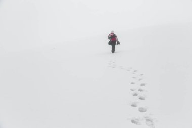 Photographer climbs the snow-covered slope of the mountain with the equipment in the fog. Footprints in the snow.