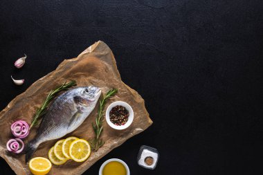 Çiğ Dorado Balığı, siyah arka planda baharatlarla yemek pişirmeye hazır. Deniz ürünleri. Üst Manzara. Boşluğu kopyala.