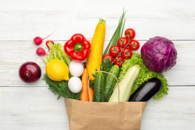 Beyaz ahşap bir arka planda kağıt bir torbada sebze ve otlar. Süpermarketten ya da marketten alışveriş yapmak. Üst görünüm.