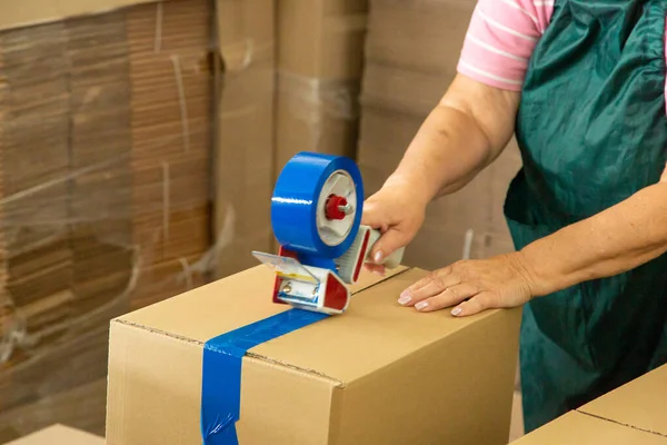 Depo çalışanı üniformalı bir kadın karton kutuyu teslimat için paketliyor..