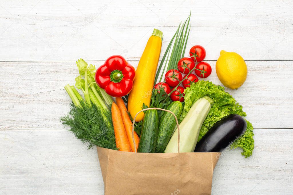 Vegetables in a paper bag on a white wooden background. Shopping in a supermarket or market.