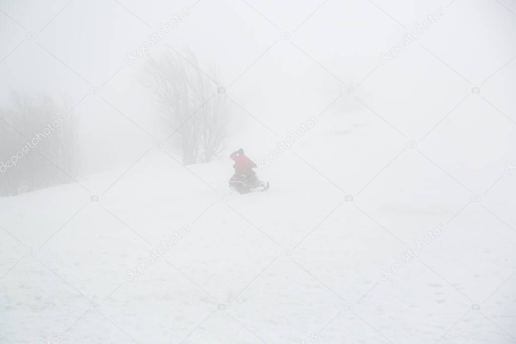 Snowmobile rider goes uphill in foggy weather.