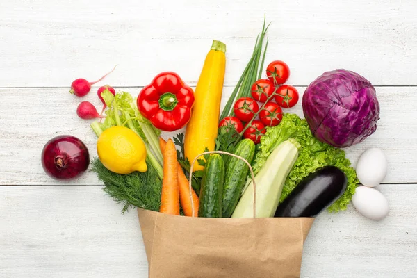 Beyaz ahşap bir arka planda kağıt bir torbada sebze ve otlar. Süpermarketten ya da marketten alışveriş yapmak. Üst görünüm.