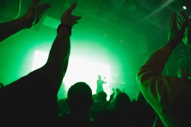 Mavi ışıklı ve enerjik atmosferli bir konser sırasında hayranlar el kaldırıyor..