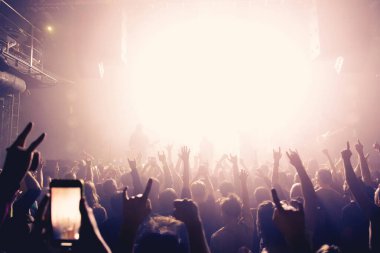 Seyirciler, enerjik atmosferli canlı bir konser sırasında yoğun sahne aydınlatmasına doğru el kaldırıyor..