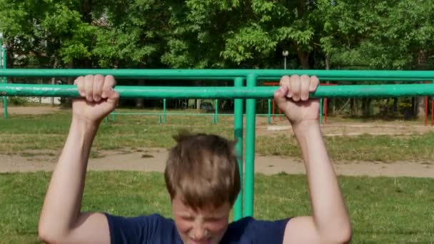 Een leuke jongen trekt zich omhoog op een horizontale balk. — Stockvideo