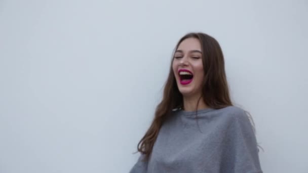 Vacker flicka skrattar hårt på en grå bakgrund. — Stockvideo