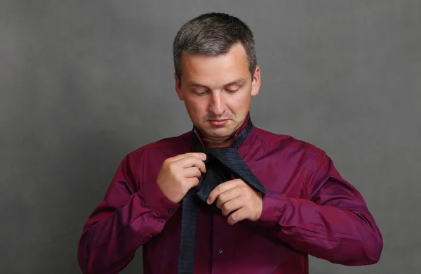 Uroczy mężczyzna w czerwonej koszuli wiąże niebieski krawat. — Zdjęcie stockowe