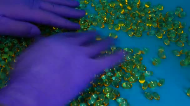 Руки в синих перчатках выбирают над капсулами рыбьего жира Мужские перчатки руки выбирают желтые капсулы на синем фоне. — стоковое видео