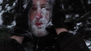 Siyah şapkalı ve eldivenli bir adam yüzünü karla yıkıyor..