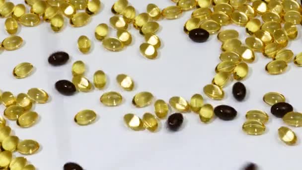 Yellow and brown fish oil capsules fall onto the white surface. — Stock Video