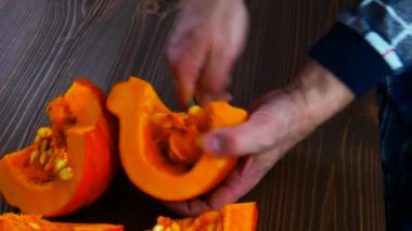Male hands are cutting a piece of pumpkin with a knife on a wooden board.