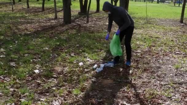 Voluntario adolescente colecciona basura en el parque en una bolsa de plástico verde. — Vídeo de stock