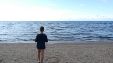 Mavi tişörtlü bir çocuk denize doğru yürüyor..