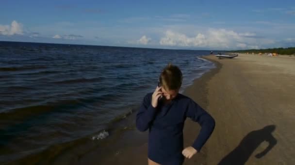 Egy 9-12 éves fiú beszél egy okostelefonon a tenger mellett.. — Stock videók