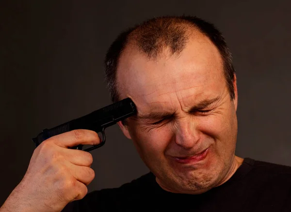 Un hombre con los ojos cerrados sostiene una pistola en su sien. — Foto de Stock