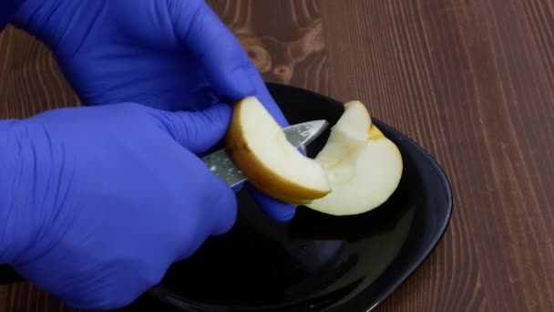 Mãos em luvas azuis estão cortando um pedaço de maçã. — Vídeo de Stock
