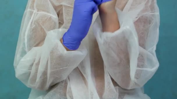 A young man in a medical gown puts on blue protective gloves. — Stock Video