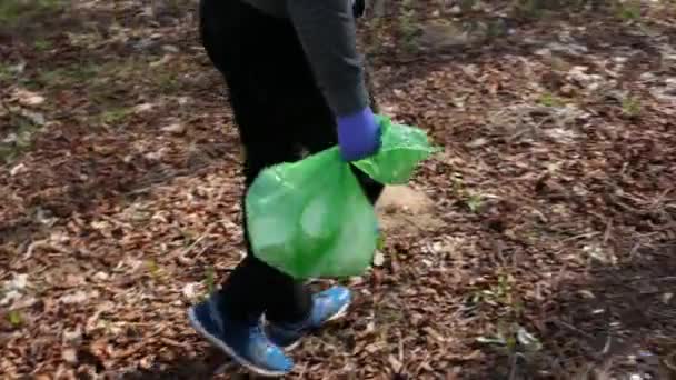 Un adolescente lleva una bolsa de basura verde después de limpiar en el bosque. — Vídeo de stock