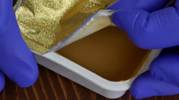 Hände in blauen Gummihandschuhen packen ein Päckchen Erdnussbutter aus. — Stockvideo