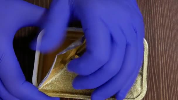 Handen in rubberen handschoenen open een klein pakje notenboter. — Stockvideo