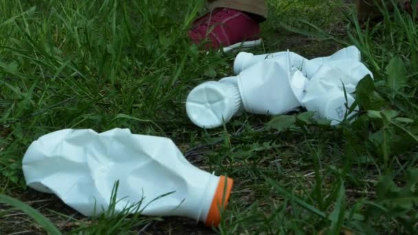 . Guantes manos recogiendo botellas de plástico blanco acostado en la hierba verde. — Vídeos de Stock