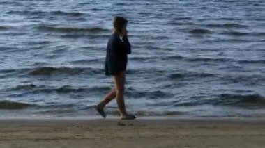 Gündüz vakti plajda bir çocuk. Denizde yürüyen bir genç.