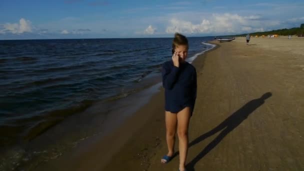 En tonårspojke går med sin telefon på stranden. — Stockvideo