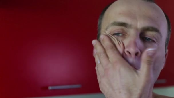 Een man van 40-45 jaar oud smeert zijn gezicht met crème na het scheren. — Stockvideo