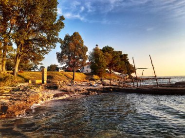 Deniz kenarındaki günbatımının dingin güzelliğini tecrübe edin, büyüleyici bir deniz feneriyle tamamlanmış, huzurlu tatillerin ve huzurlu sahil kaçışlarının anılarını canlandıran.