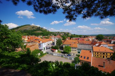 Avrupa 'nın güneş ışığıyla yıkanmış pitoresk bir şehir manzarası keşfedin. Terracotta çatıları olan tarihi binalar canlı mavi gökyüzünün altında yuvarlanan yeşil tepelere yuva yapar. Yolculuk için mükemmel bir ilham kaynağı..