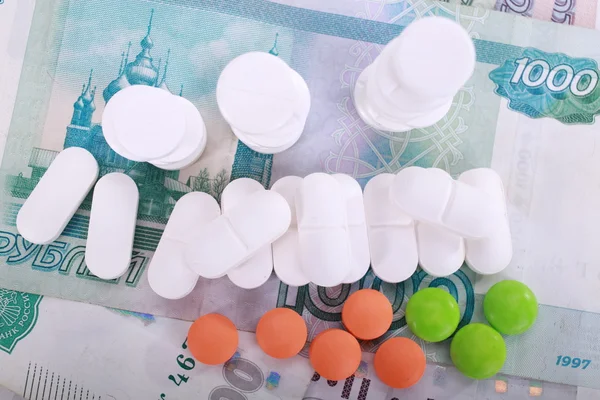 Tabletki o różnych kolorach na tle pieniędzy. — Zdjęcie stockowe