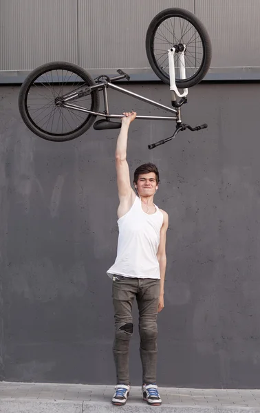 Menino com bicicleta de prata sobrecarga no fundo da parede cinza — Fotografia de Stock
