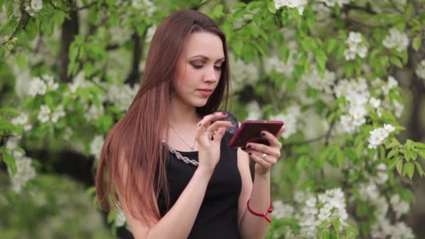 A menina com um smartphone nas mãos de no jardim — Vídeo de Stock