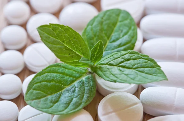 Different white pills and foliage mint on a wooden background — Stock Photo, Image