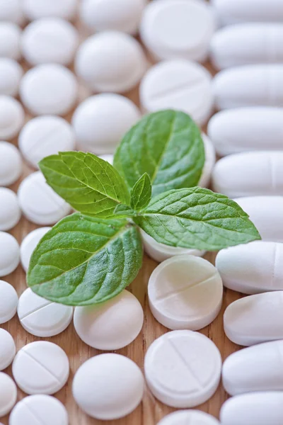 Different white pills and foliage mint on a wooden background — Stock Photo, Image