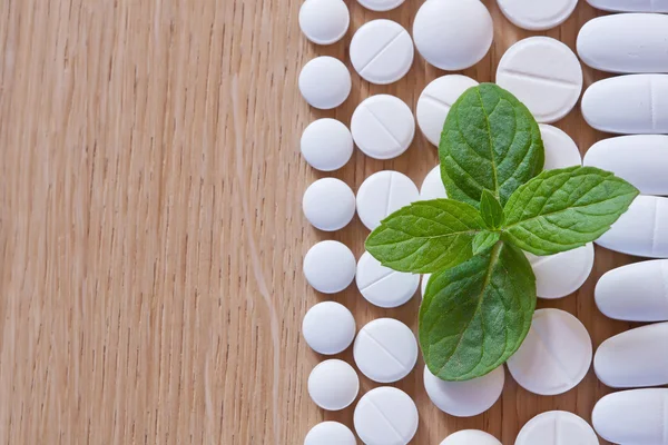 White pills and foliage mint on a wooden background — Stock Photo, Image