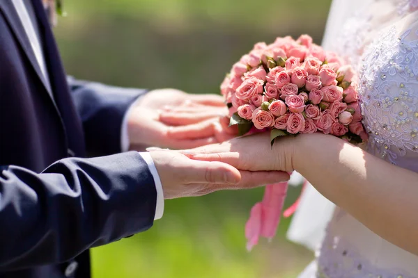 Hands of bride and groom holding a bouquet of pink roses — Stock Photo, Image