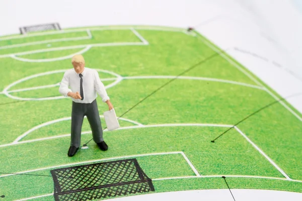 Miniature figurine of a football coach teaching a green football field — Stock Photo, Image