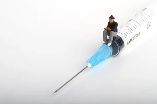 Miniatuur beeldje van een persoon zittend op een grote injectiespuit: therapie of drug verslaving concept. — Stockfoto