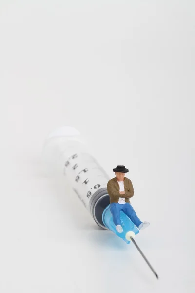 Miniature figurine of a person sitting on a big syringe : therapy or drug addiction concept. — Stock Photo, Image