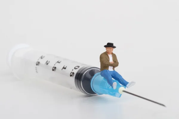Miniaturfigur einer Person, die auf einer großen Spritze sitzt: Therapie- oder Drogenabhängigkeitskonzept. — Stockfoto