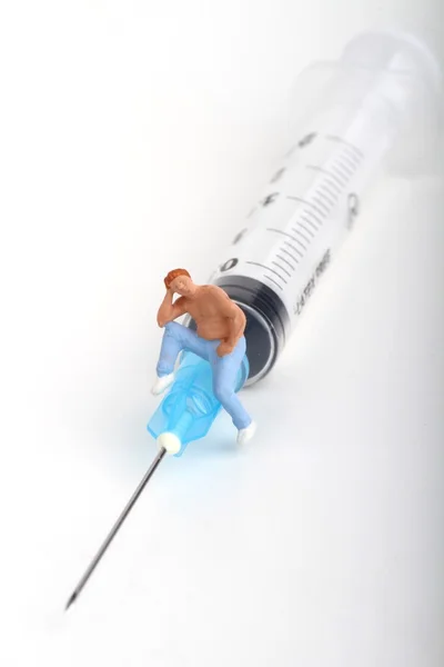 Miniatuur beeldje van een persoon zittend op een grote injectiespuit: therapie of drug verslaving concept. — Stockfoto